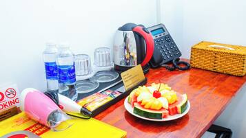 A desk with a phone, water bottles, a hairdryer, a plate of fruit, and a basket.