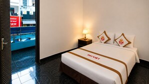 A hotel room with a bed, a nightstand, a lamp, and a view of a building outside. - The Rice Hotel & Tour - 131 Bui Vien (Ho Chi Minh City)