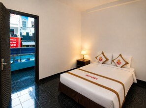 A hotel room with a bed, a nightstand, a lamp, and a view of a building outside. - The Rice Hotel & Tour - 131 Bui Vien (Ho Chi Minh City)