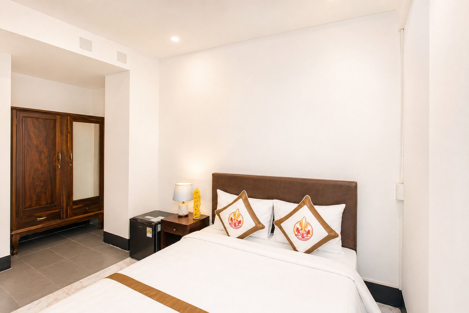Una habitación de hotel con cama, mesita de noche, lámpara, armario y puerta.