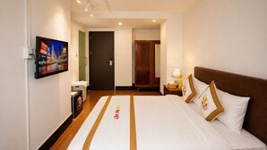 A hotel room with a bed, a nightstand, a lamp, a TV mounted on the wall, and a door leading to another room. - The Rice Hotel & Tour - 131 Bui Vien (Ho Chi Minh City)