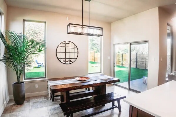 Une cuisine moderne avec une table en bois, une grande plante en pot et une vue sur le jardin à travers une porte-fenêtre coulissante.