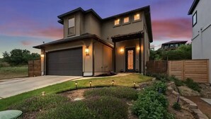 A modern two-story house with a garage, a well-maintained lawn, and a garden with various plants and flowers. - New Lake Travis Retreat Home . Mt View . 3 bd 3 ba (Austin)