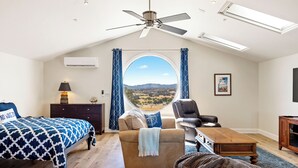 A bedroom with a bed, a sofa, a chair, a desk, and a view of the outdoors.