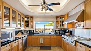 A kitchen with wooden cabinets, a black countertop, stainless steel appliances, and a view through the window.