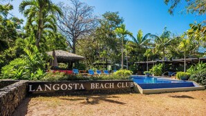 A beach club with a sign reading "LANGOSTA BEACH CLUB," a pool, lounge chairs, and tropical vegetation. - Boho House: Tamarindo Beach (Tamarindo)