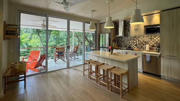 A modern kitchen with a large island, bar stools, and a view of the outdoors. - Boho House: Tamarindo Beach (Tamarindo)