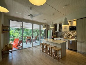 Une cuisine moderne dotée d’un grand îlot central, de tabourets de bar et offrant une vue sur l’extérieur.