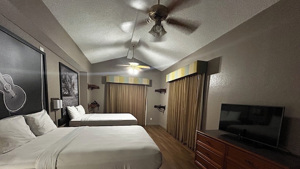 A hotel room with two beds, a ceiling fan, a TV, and a wooden dresser.