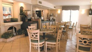 A dining area with round tables and chairs, a bar area with a counter and various appliances, and a fireplace with decorative items.
