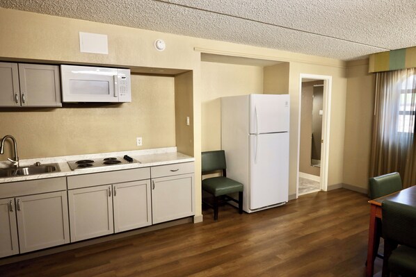 A compact kitchen with a microwave, stove, sink, and cabinets. There is a refrigerator and a dining area with chairs. - Studio with two queen beds- non smoking (Austin)