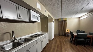 A compact kitchen with a sink, stove, and microwave. There is a dining area with a table and chairs.