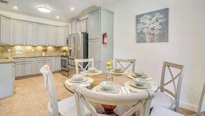 Cozinha moderna com armários brancos, bancadas de granito e uma área de refeições com mesa redonda para seis pessoas.