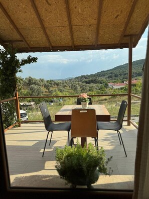 An outdoor patio with a table and chairs, overlooking a scenic landscape with hills and trees. - ÖZLEMKÖY (Seferihisar)