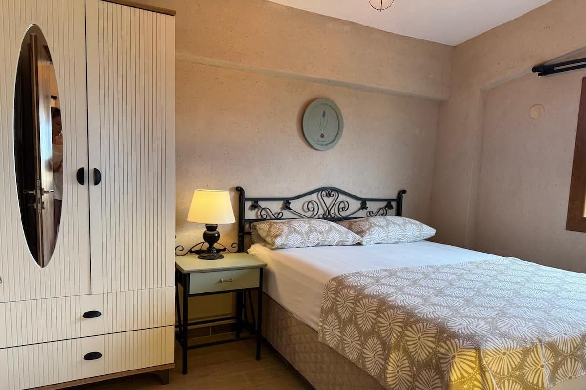 Ein Schlafzimmer mit Bett, Nachttisch mit Lampe, Kleiderschrank und Wanduhr.