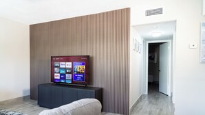 A modern living room with a flat-screen TV mounted on a wall, a grey sofa, and a patterned rug. - Delray Ocean Breeze (Delray Beach)
