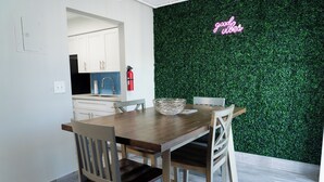 A modern kitchen with white cabinets, a wooden dining table, and a green wall with a neon sign. - Delray Ocean Breeze (Delray Beach)