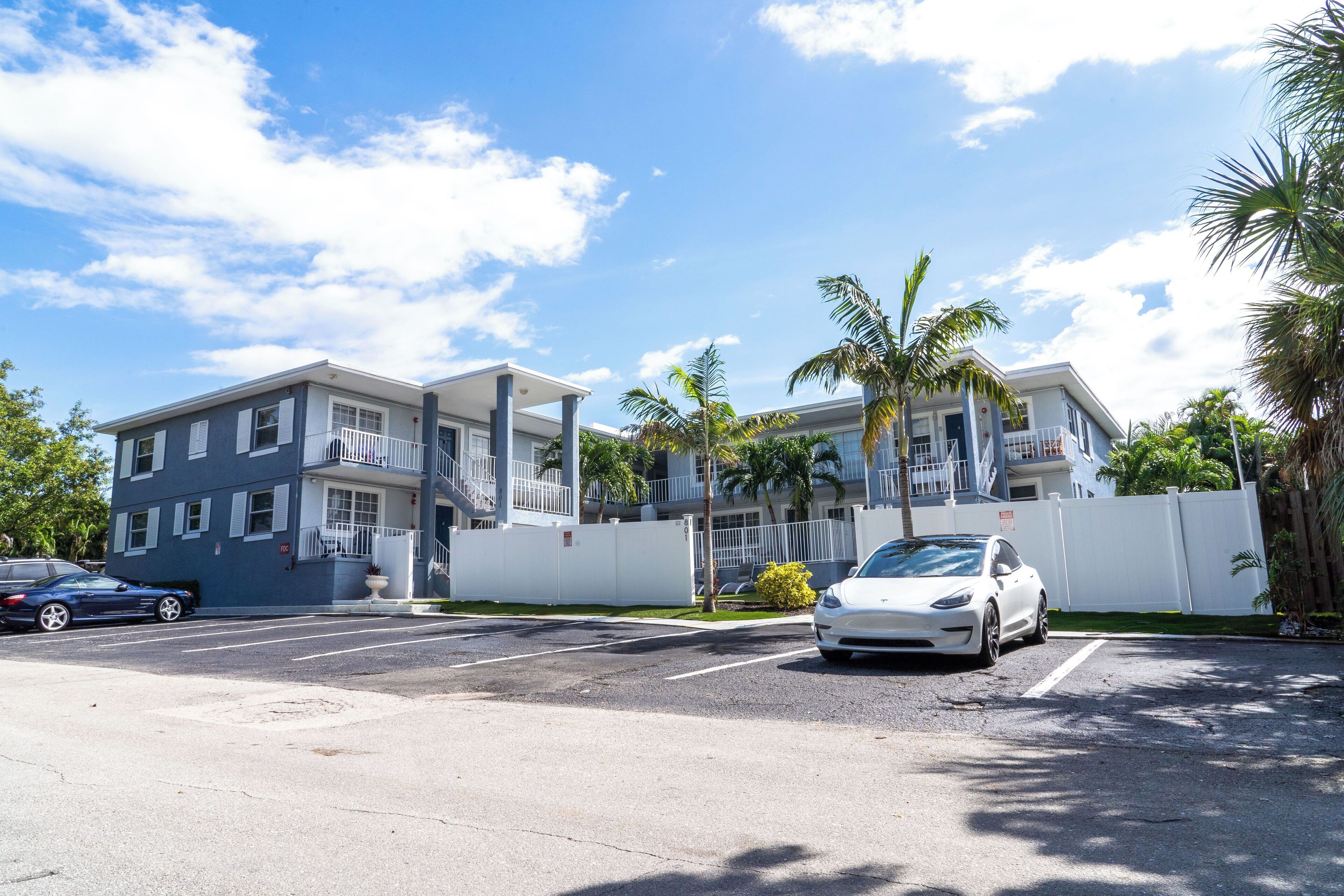 Un edificio moderno con estacionamiento, un coche blanco y palmeras.