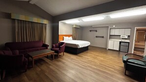 Ein Hotelzimmer mit Bett, Sofa, Schreibtisch, Stuhl, Küchenzeile und Badezimmer.