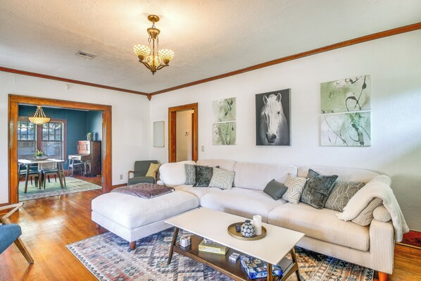 A living room with a sectional sofa, a coffee table, and a dining area visible through an open doorway. - Historic Craftsman Home 3 Mi to Fort Sill N Lawton (Lawton)