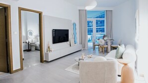 Un salon moderne doté d’un téléviseur à écran plat, d’un coin repas avec une table et des chaises, et d’une grande fenêtre agrémentée de rideaux.