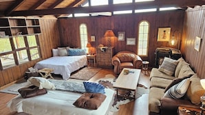 A cozy, rustic room with wooden walls and a high ceiling. It features two beds, a leather armchair, a sofa, and a small table. - Historic Dude Ranch Rustic Cowboy Cabin Desert Experience (Tucson)