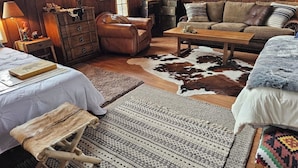 A cozy room with a wooden floor, a leather sofa, a wooden coffee table, and a cowhide rug. - Historic Dude Ranch Rustic Cowboy Cabin Desert Experience (Tucson)
