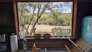 A kitchen with a sink, faucet, and window overlooking a desert landscape. - Historic Dude Ranch Rustic Cowboy Cabin Desert Experience (Tucson)