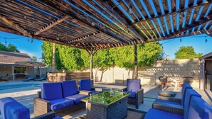 An outdoor patio area with wicker furniture, a glass-top table, and a pergola overhead. - Backyard Paradise in Chandler (Chandler)