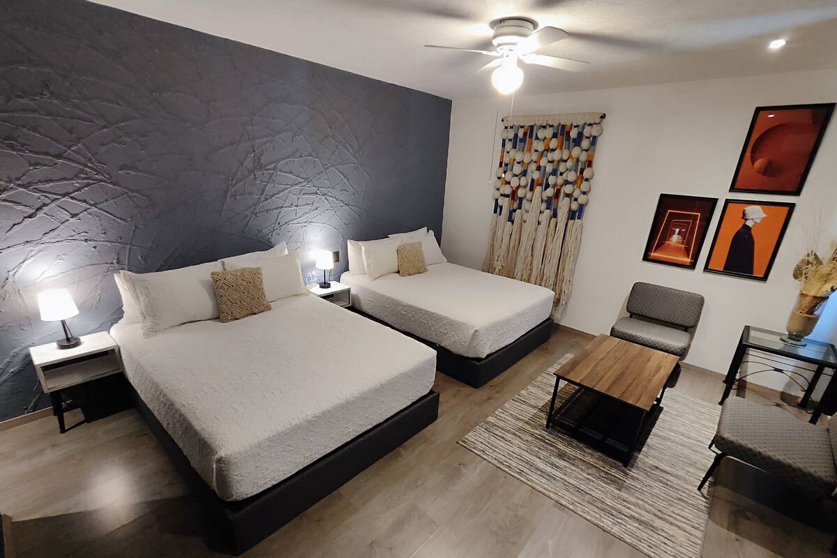 A modern hotel room with two beds, a ceiling fan, a small table, and a seating area.