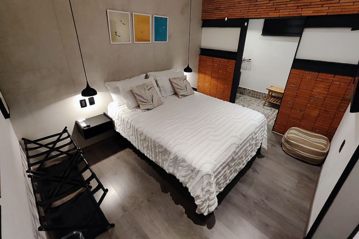 A modern bedroom with a large bed, a wooden accent wall, and a small seating area.