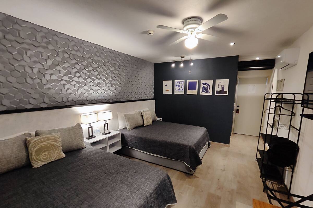 A bedroom with two beds, a ceiling fan, wall-mounted artwork, and a black metal shelf.
