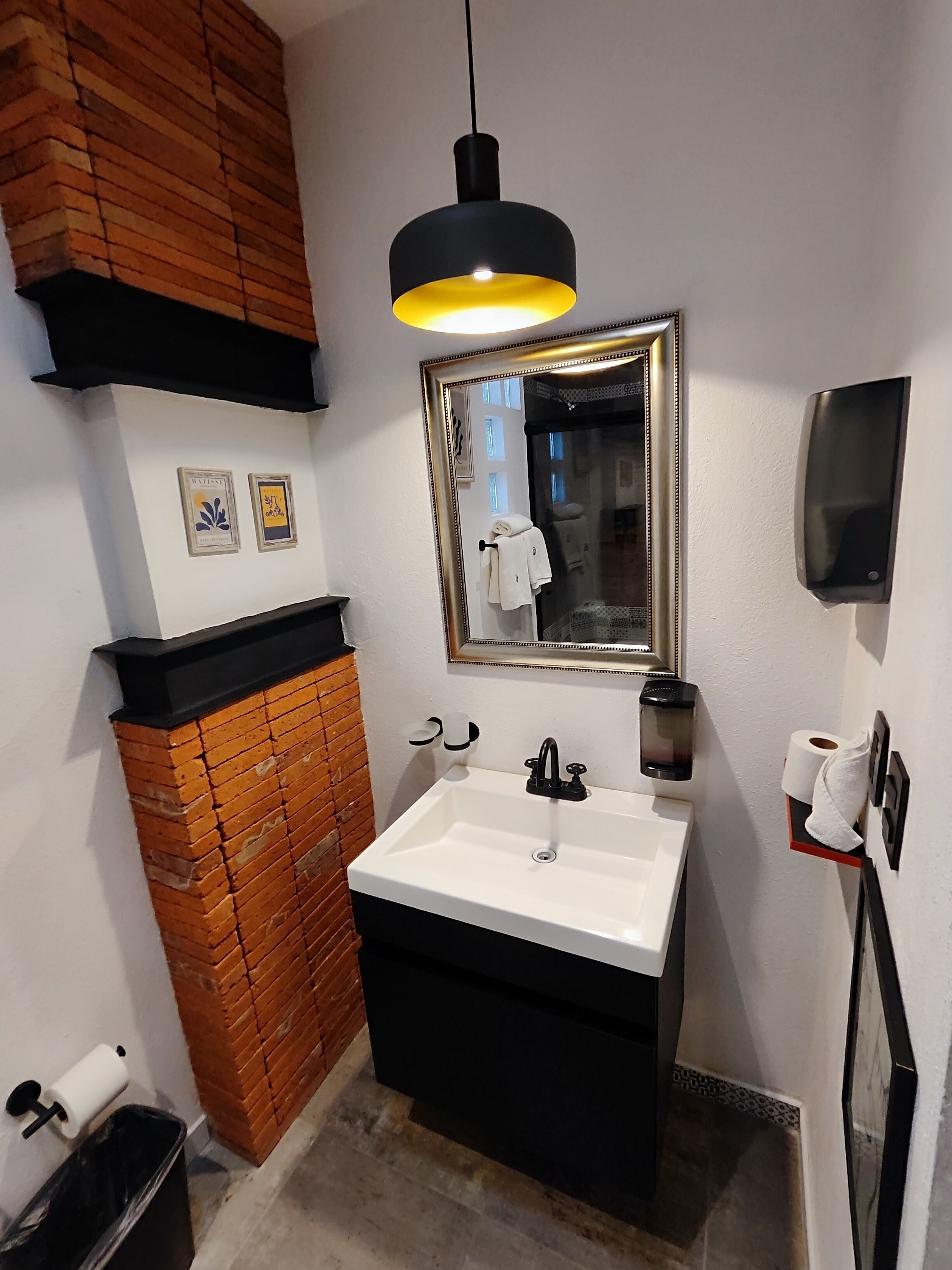 A bathroom with a white sink, black vanity, wooden wall paneling, a mirror, and a hanging light fixture.