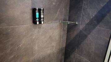 A bathroom with dark tiles, a shower, a glass door, and a blue bowl on the floor.