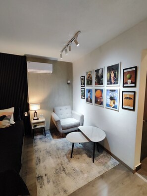 A modern living room with a sofa, a white armchair, a small table, and a rug. There are framed pictures on the wall and an air conditioning unit on the ceiling. - Casa Aceves & Bueno Hotel Boutique (El Salto)