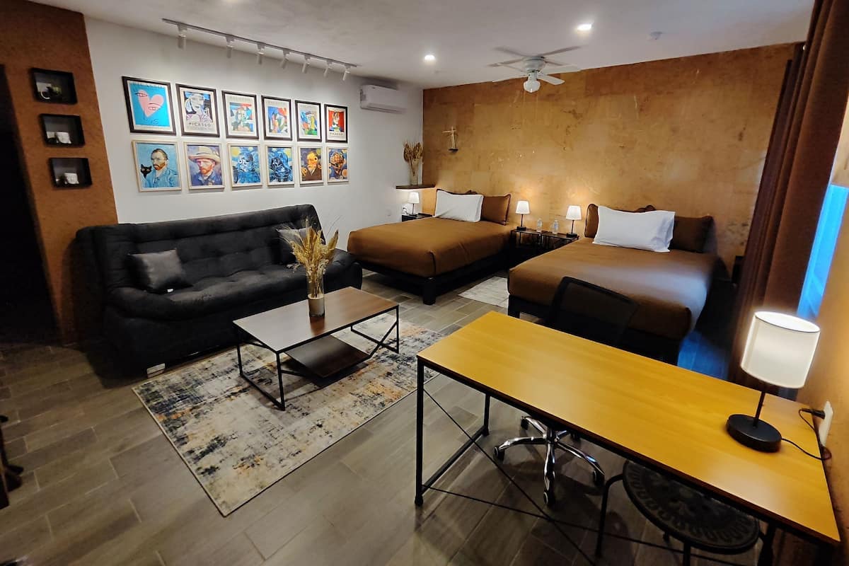 A hotel room with a sofa, two single beds, a small table, and a ceiling fan.