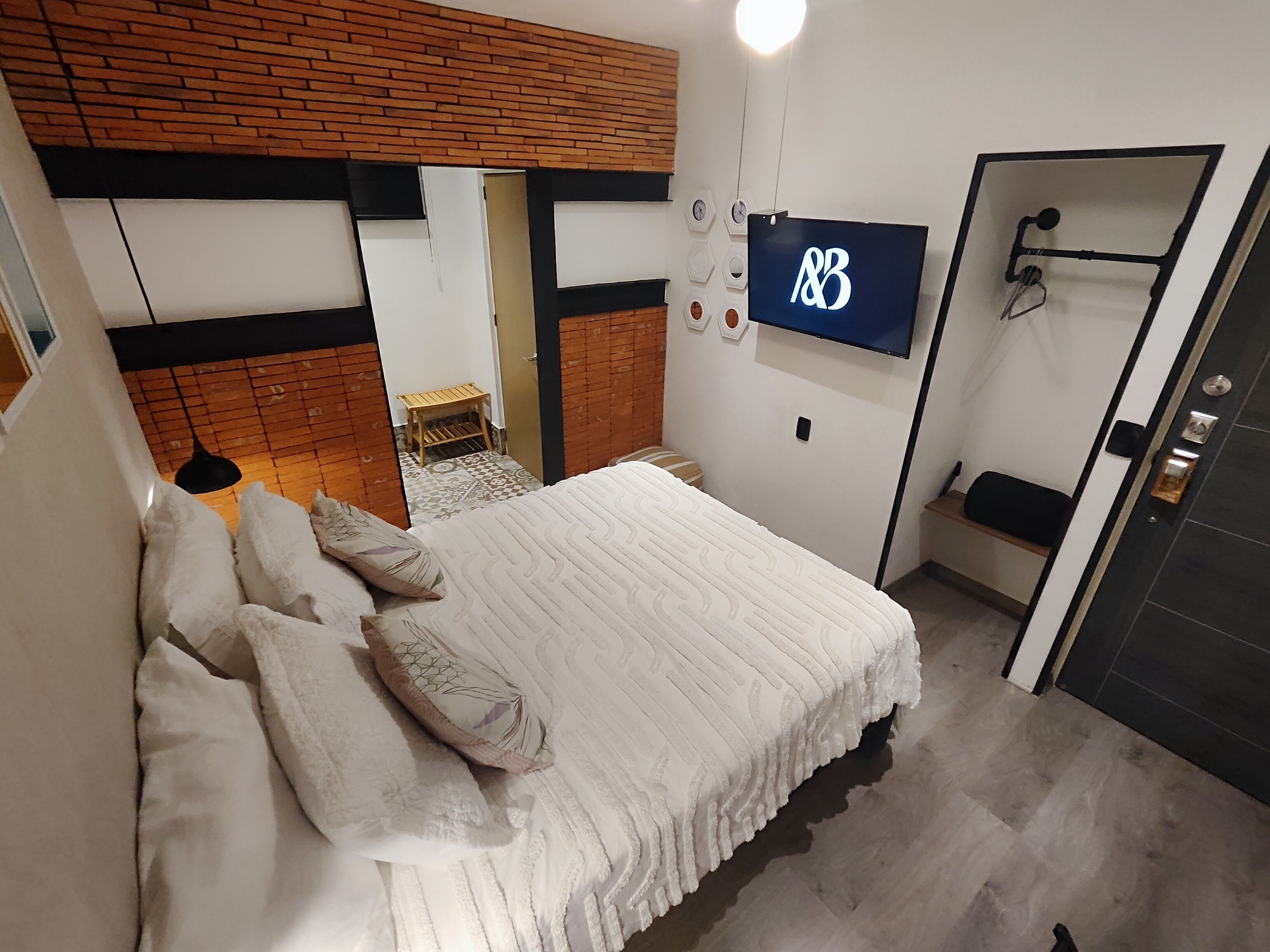 A modern bedroom with a large bed, a TV mounted on the wall, and a wooden bench.