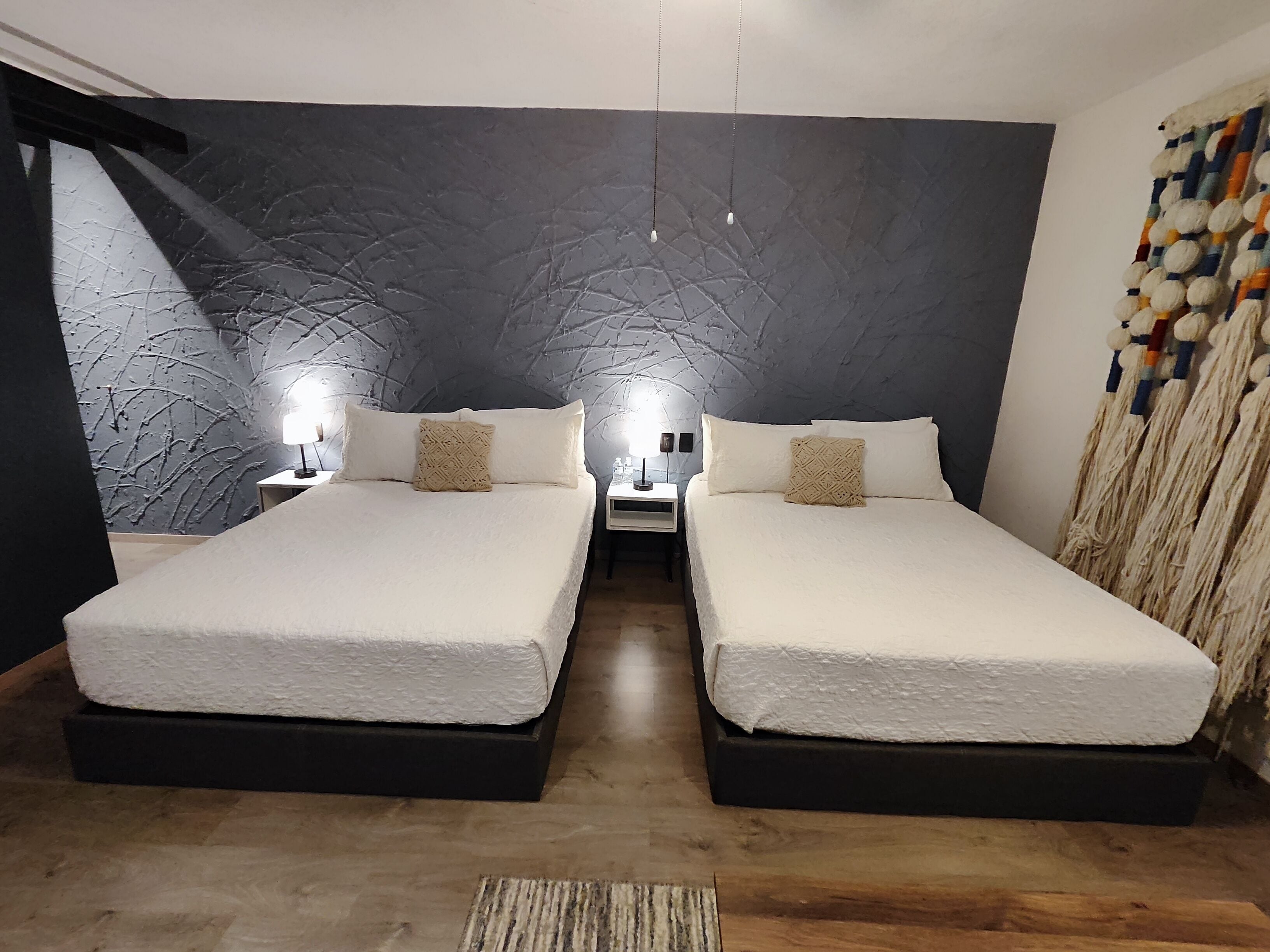 A double room with two beds, a textured wall, a hanging light fixture, and a patterned curtain.