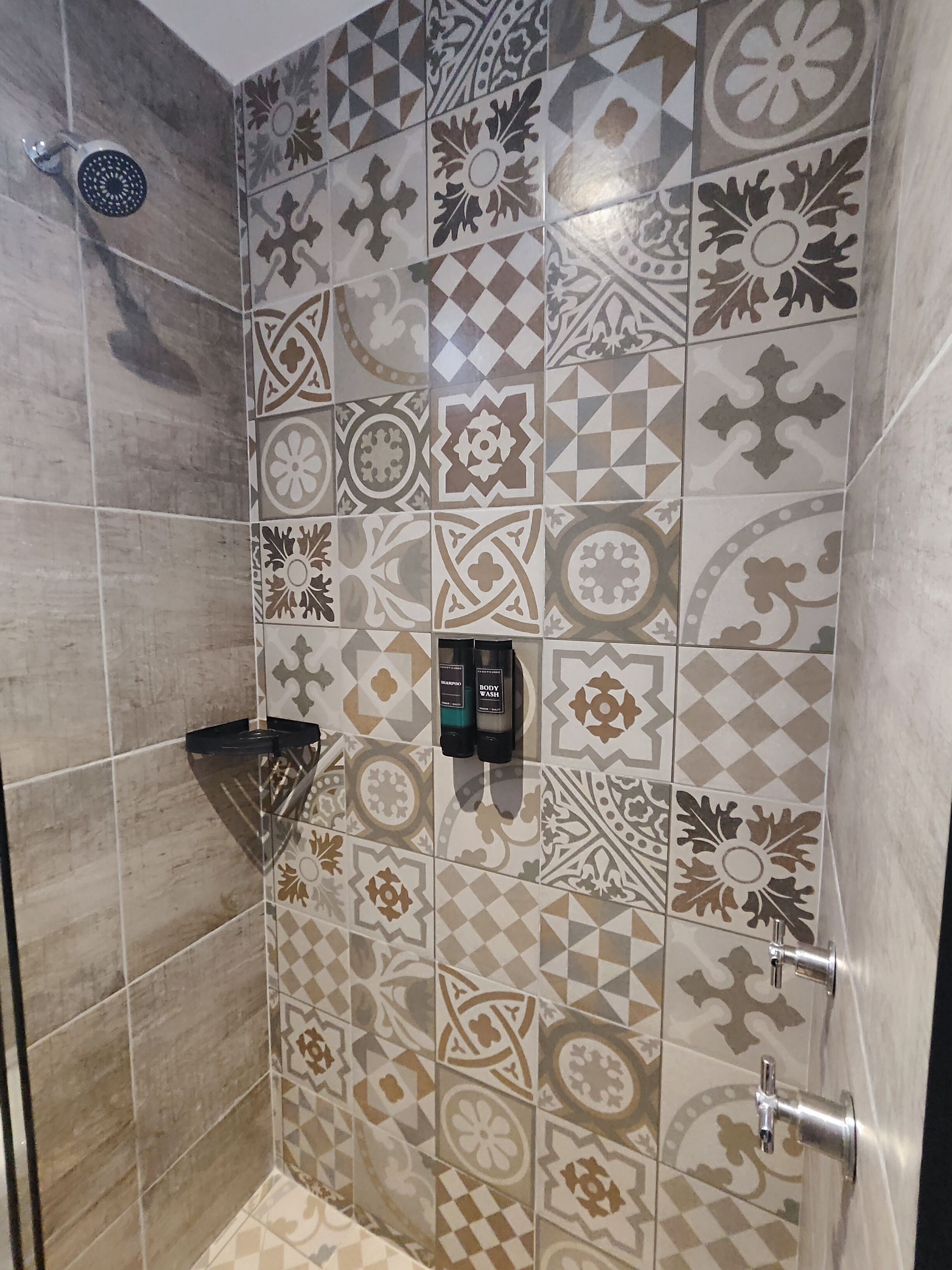 Area doccia con piastrelle decorate, soffione a mano e dispenser di sapone.