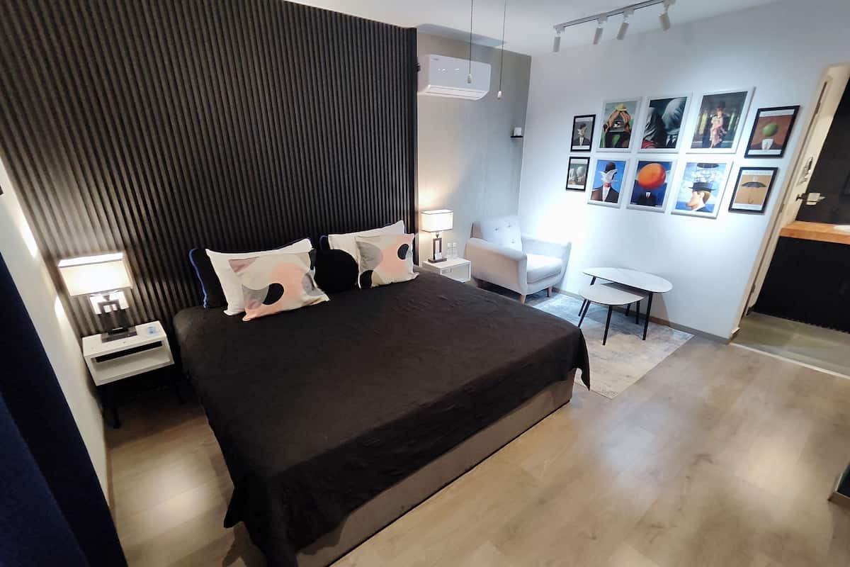 A modern hotel room with a large bed, a desk, a chair, and a small table.