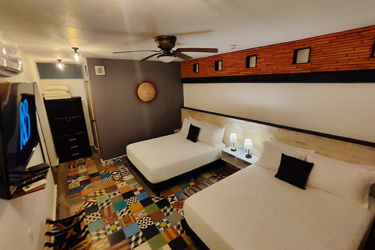 A hotel room with two beds, a ceiling fan, a patterned floor, and a television.