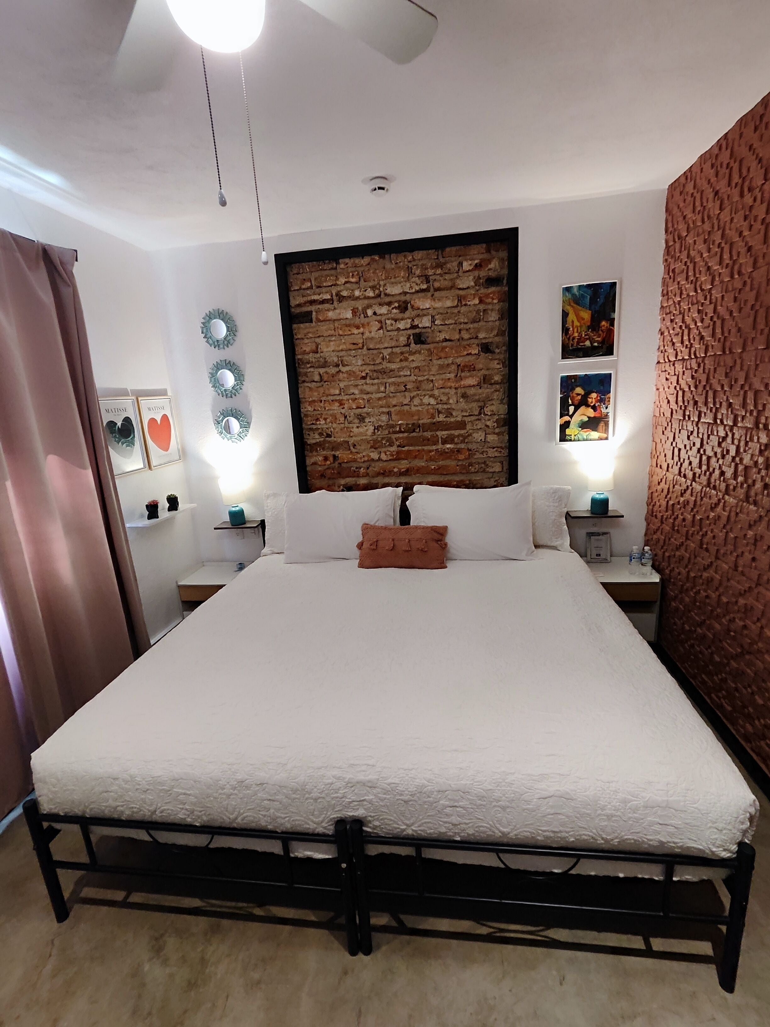 Une chambre avec un grand lit, un mur décoré d’un motif en briques et un ventilateur de plafond.
