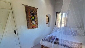 Un dormitorio con cama bajo dosel, alfombra de cuero de vaca, tapiz en la pared y una puerta con pomo.