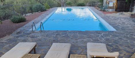 A pool area with lounge chairs and a wooden table under a canopy.