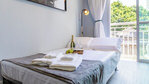 A neatly made bed with a blanket, a bottle of champagne, and glasses on a tray, a painting on the wall, and a view of greenery outside. - Apt piscina e AC com academia e vaga (São Paulo)