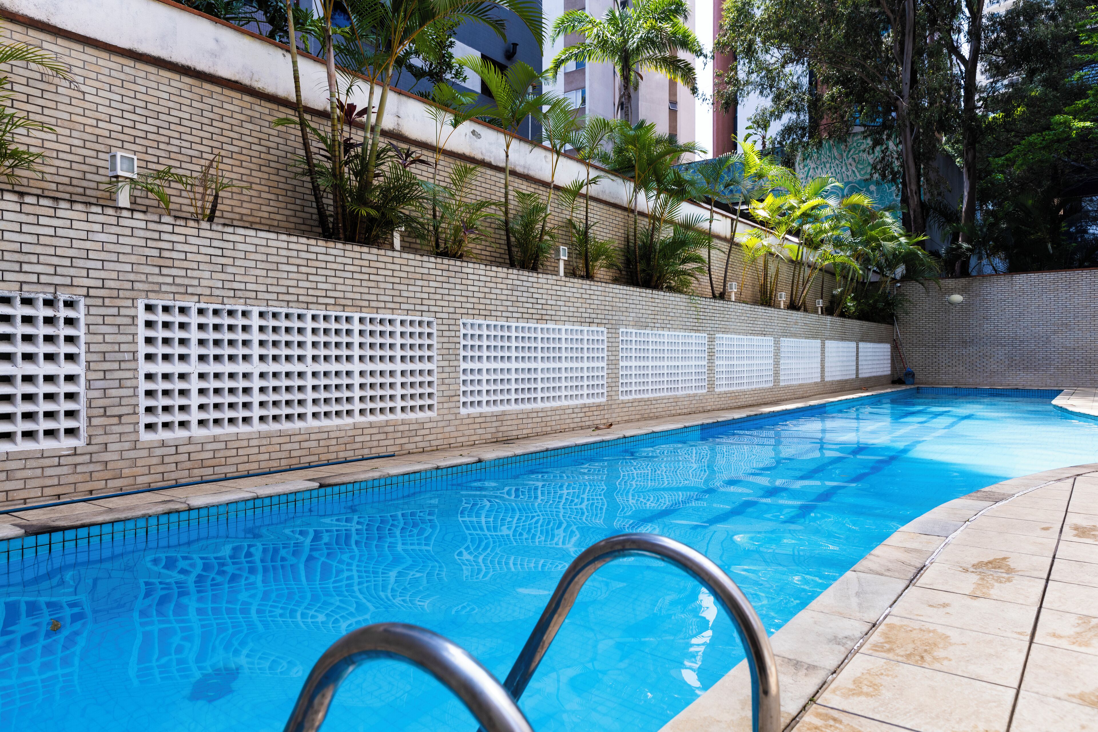 A swimming pool with a tiled edge, surrounded by a brick wall and a metal fence.