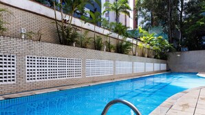 A swimming pool with a tiled edge, surrounded by a brick wall and a metal fence. - Apt piscina e AC com academia e vaga (São Paulo)