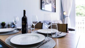 A dining table set with plates, glasses, and a bottle of wine, with a view of a balcony and a framed picture on the wall. - Apt piscina e AC com academia e vaga (São Paulo)