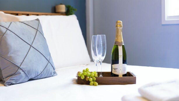 A bed with a pillow, a tray with a bottle of champagne, two glasses, and a bunch of grapes. - Apt piscina e AC com academia e vaga (São Paulo)