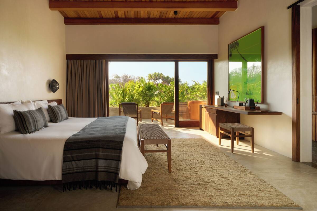 A bedroom with a bed, a desk, and a view of greenery.